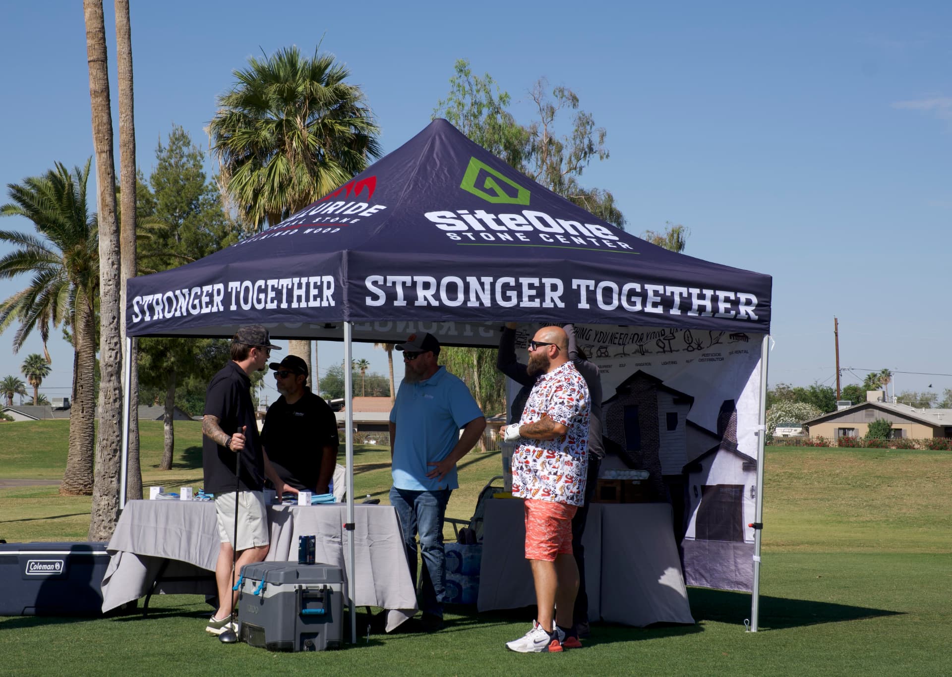 Sponsors talking with golfers under a branded SHA sponsor tent on the course