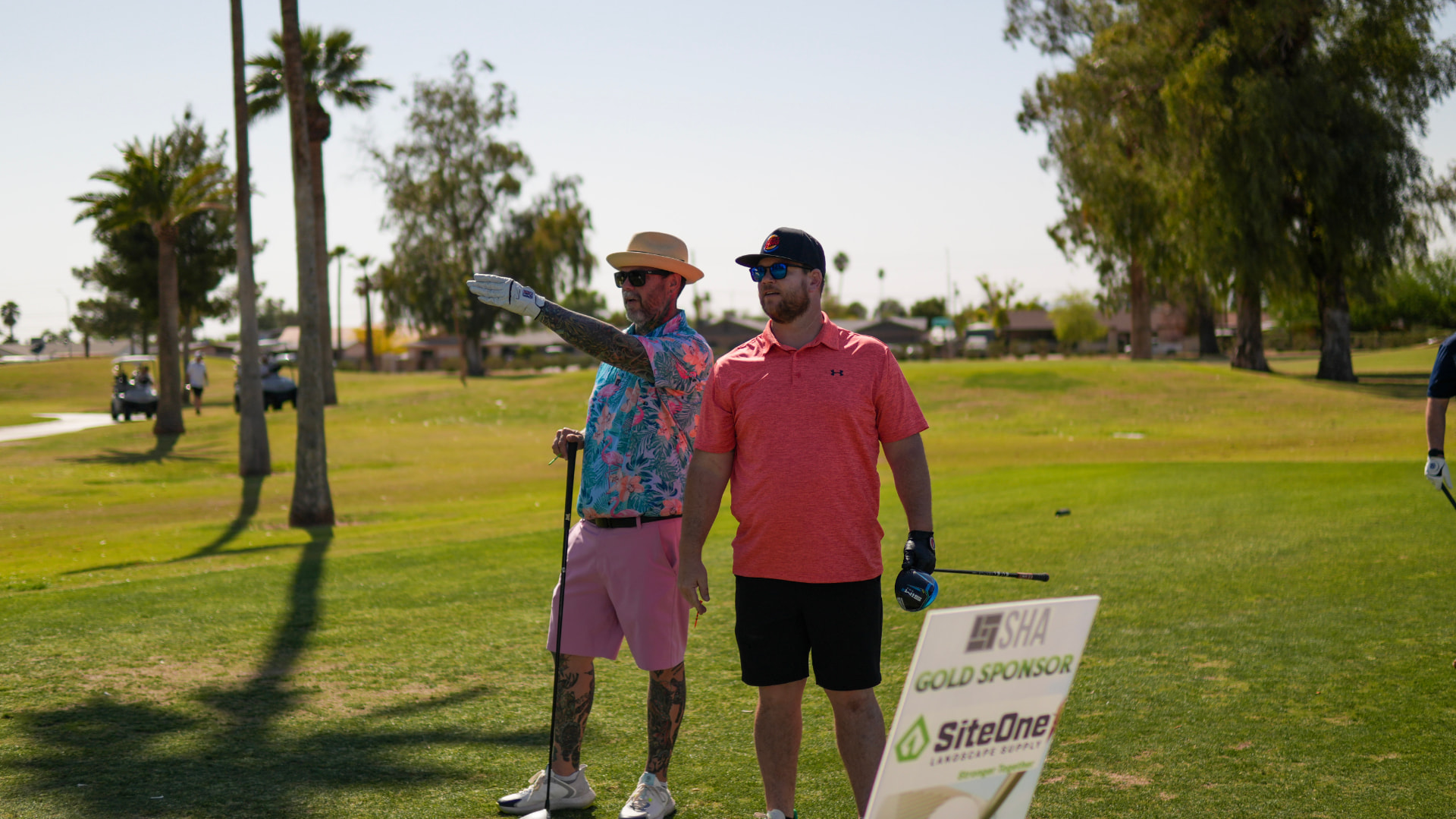 Two SHA members sizing up a tee shot next to a gold sponsor sign at the SHA Golf Tournament