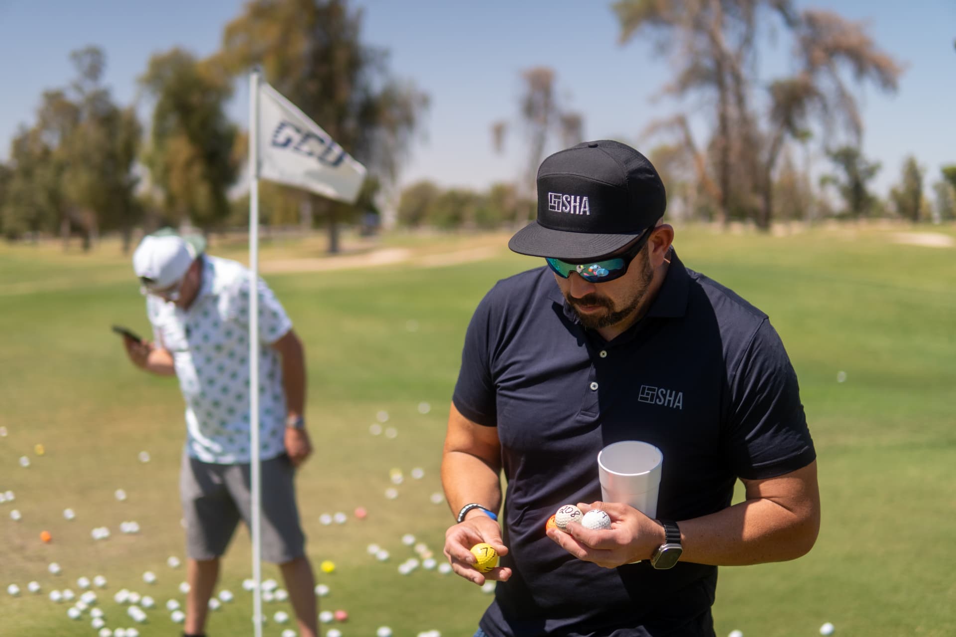 An SHA member in a branded hat and polo collecting golf balls on the practice green